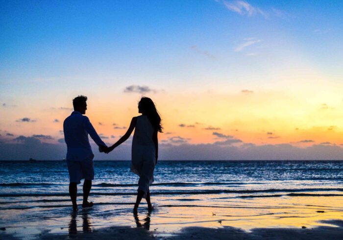 Szczęśliwa para spaceruje po plaży trzymając się za ręce