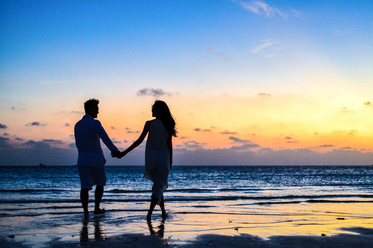 Szczęśliwa para spaceruje po plaży trzymając się za ręce